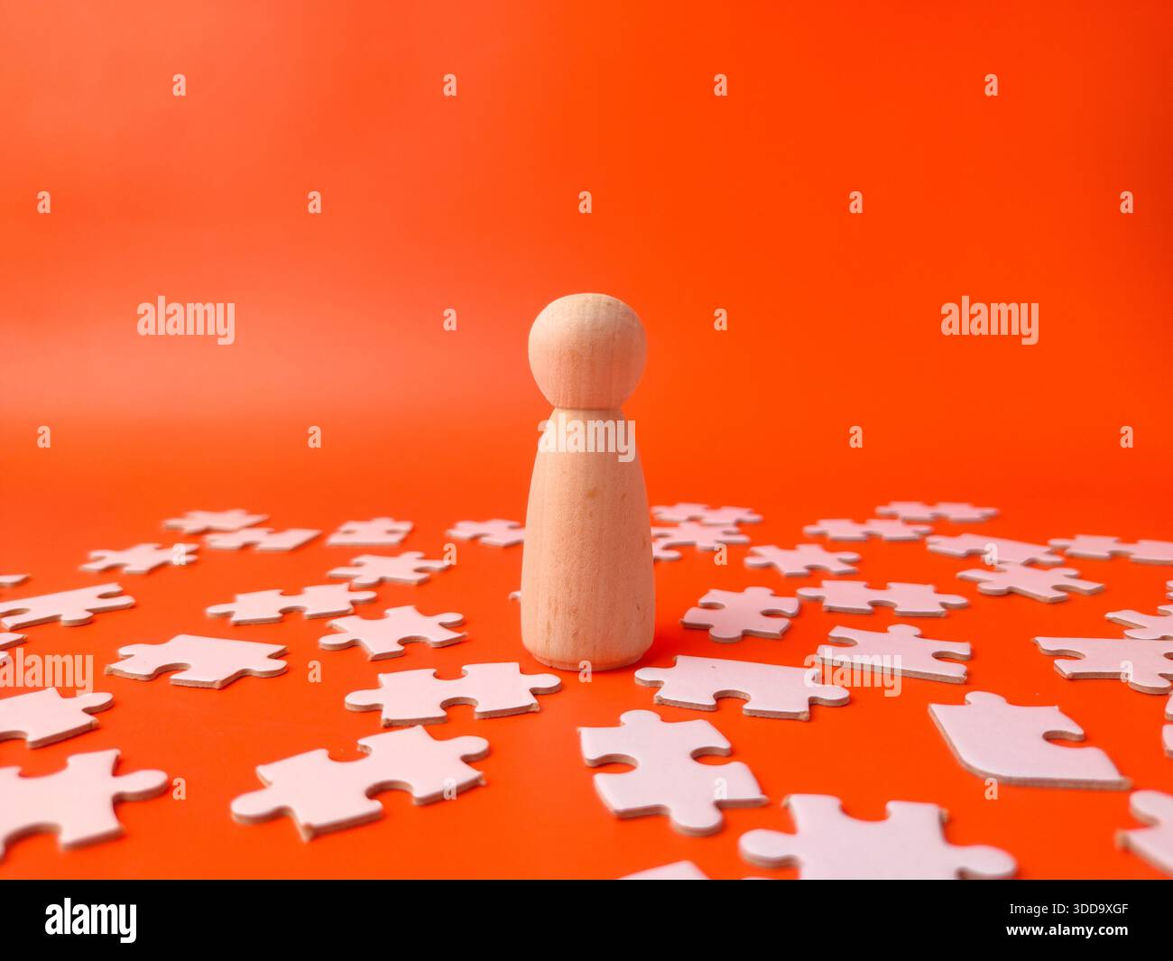 Puppe aus Holz, umgeben von weißen Puzzleteilen auf orangem Hintergrund. Stockfoto