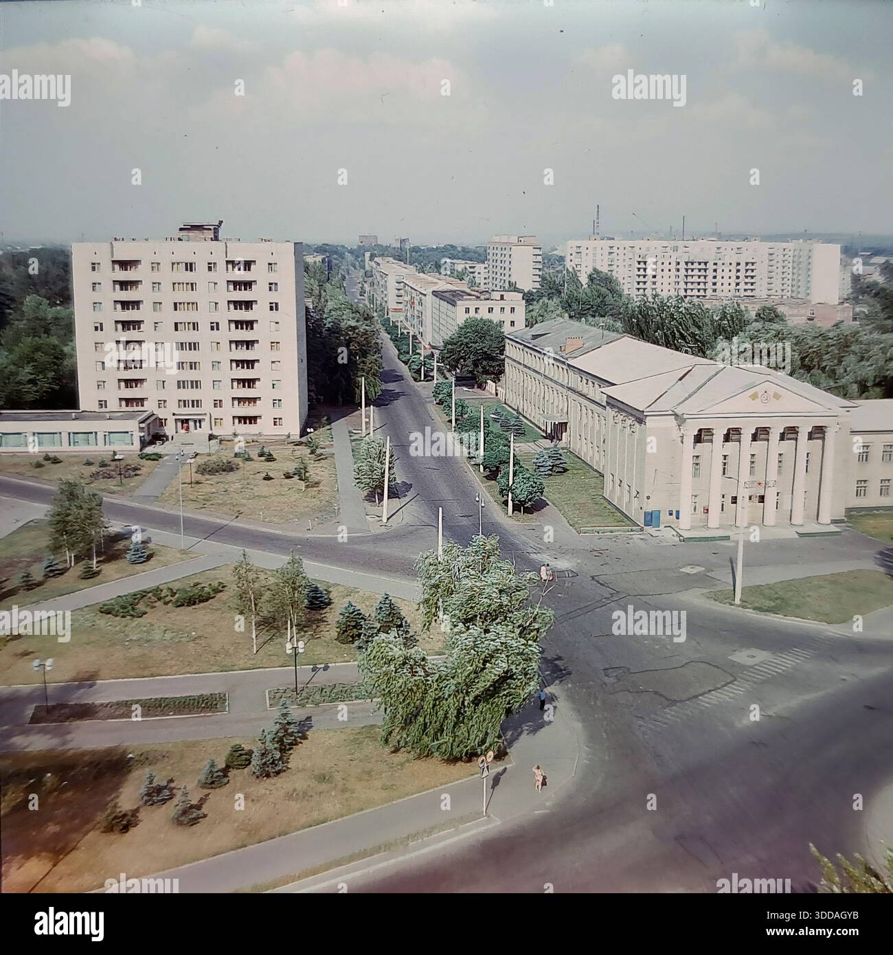 Slawjansk, Ukraine, UdSSR, 1980er Jahre Ein Panoramablick aus einem hohen Winkel mit Blick auf die landwirtschaftliche Technische Hochschule in der Chubar-Straße (heute Swetlodarskaya-Straße). Das Bildungsgebäude verfügt über einen klassischen Säulengang, der im Kontrast zum modernen neunstöckigen Wohnblock aus weißem Backstein auf der anderen Straßenseite steht. Die breiten Straßen sind ruhig mit minimalem Verkehr, umgeben von grünen Rasenflächen und jungen Tannen. Dieses Archivbild erfasst die Stadtplanung, die Bildungsinfrastruktur und die friedliche Atmosphäre der sowjetischen Donbass-Stadt. Stockfoto