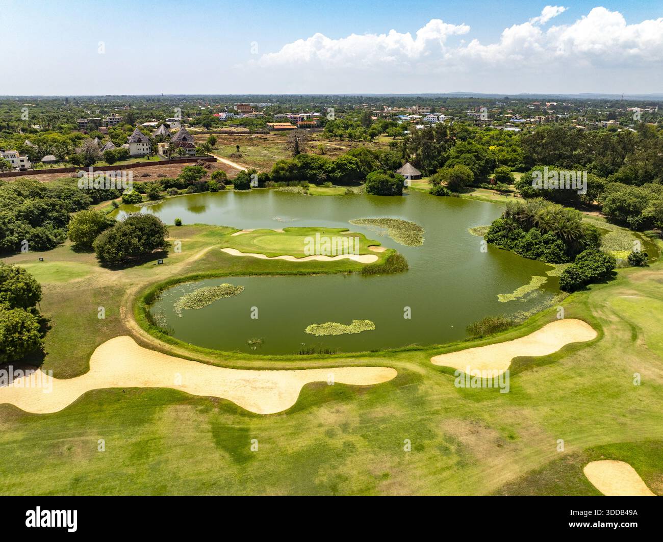 Aus der Vogelperspektive auf einen üppig grünen Golfplatz mit einem zentralen Teich, der den Himmel reflektiert, umgeben von Bäumen und Gebäuden, Küste, Kwale County, Kenia. Stockfoto