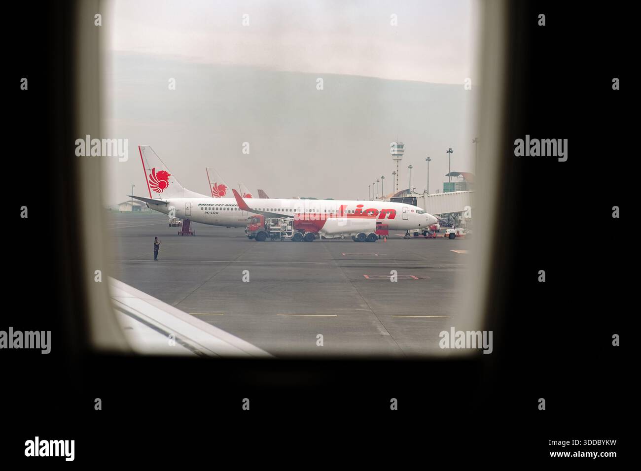 Ansicht von einem Flugzeugfenster mit mehreren Lion Air Boeing 737-900ER Flugzeugen, die auf dem Rollfeld geparkt sind. Ein Tankwagen und die Bodencrew warten ein Flugzeug. A Stockfoto