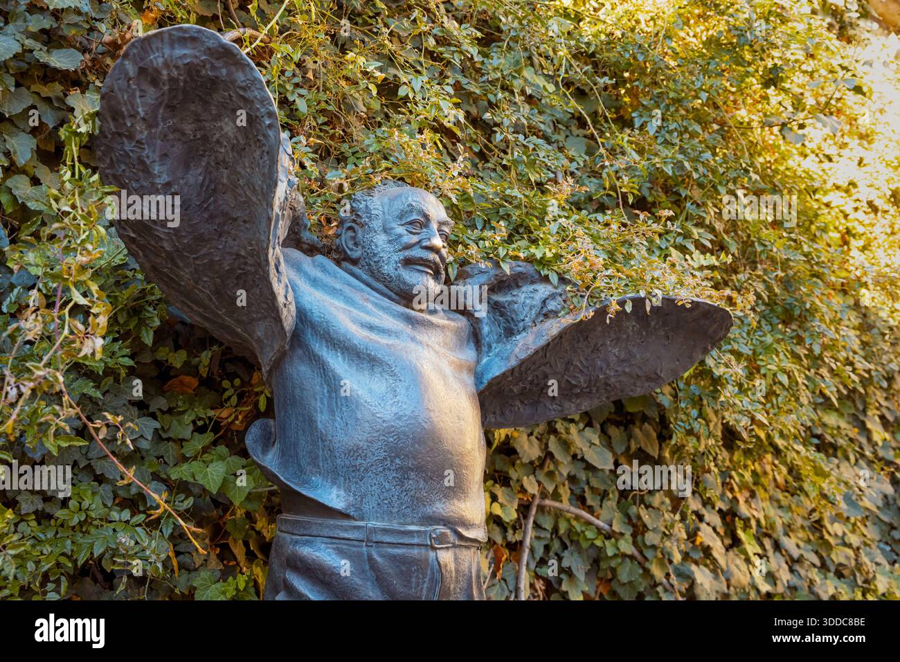 31. Oktober 2025, Tiflis, Georgien: Skulptur eines fröhlichen Mannes mit ausgestreckten Armen, umgeben von üppigem grünem Efeu Stockfoto