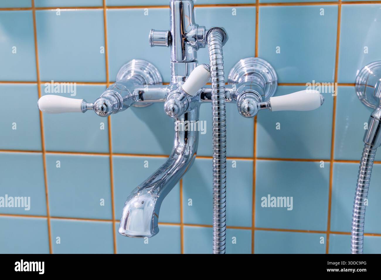 Chrom-Armatur im Vintage-Stil mit weißen Keramikgriffen an der blau gefliesten Wand im Badezimmer Stockfoto