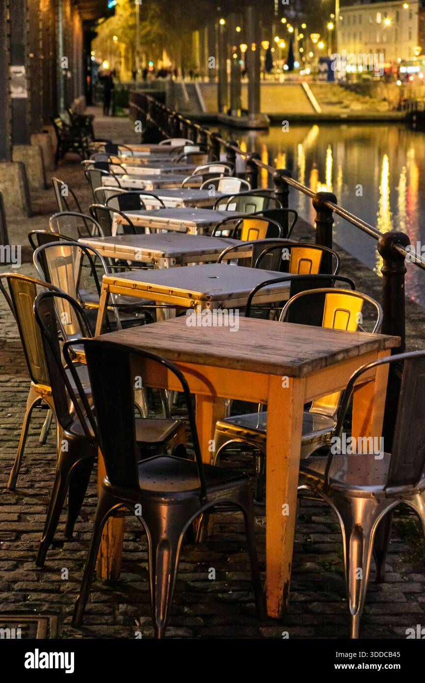 Bristol UK 12-29-2025 Leere Tische und Stühle stehen abends vor einem Restaurant, mit Reflexen der Lichter der Stadt auf dem Wasser. Stockfoto