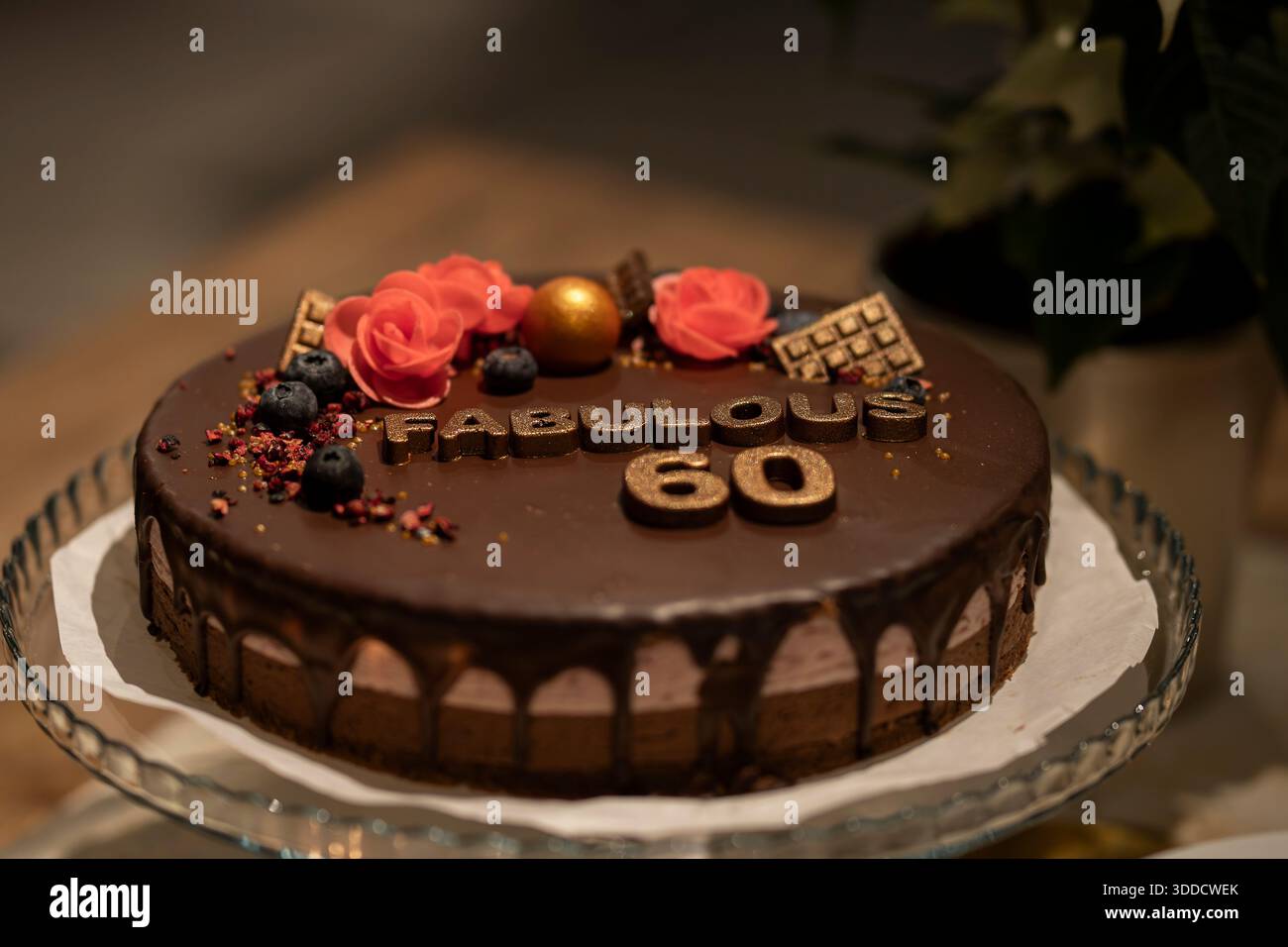 Eleganter Schokoladen-Geburtstagskuchen, dekoriert mit Blumen, Beeren und goldenen Details zum 60. Geburtstag. Luxuriöser Schokoladen-Tropfkuchen. Stockfoto