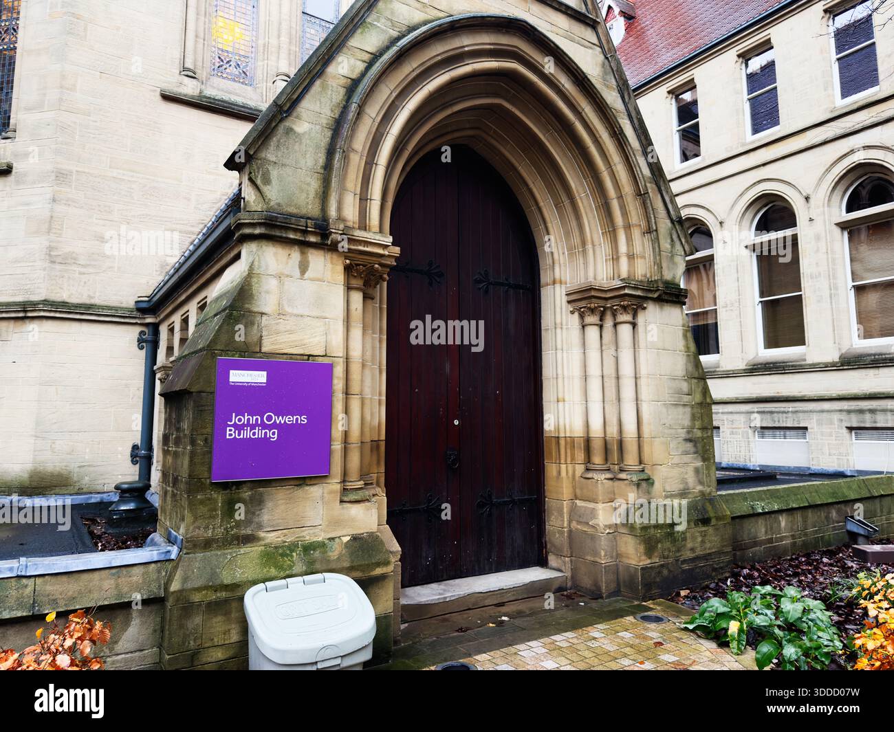 Manchester, Großbritannien - 06. Dezember 2025: Historischer Eingang zum John Owens Building auf dem Manchester Campus mit großer Holztür und lila Schild. Stockfoto