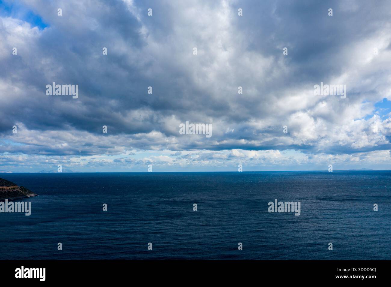 Das riesige blaue Meer erstreckt sich bis zum Horizont unter einem Himmel voller dicker, strukturierter Wolken. Die stimmungsvolle Atmosphäre wird durch das Verschieben von Licht und tiefen Schatten über dem Wasser verstärkt. Stockfoto