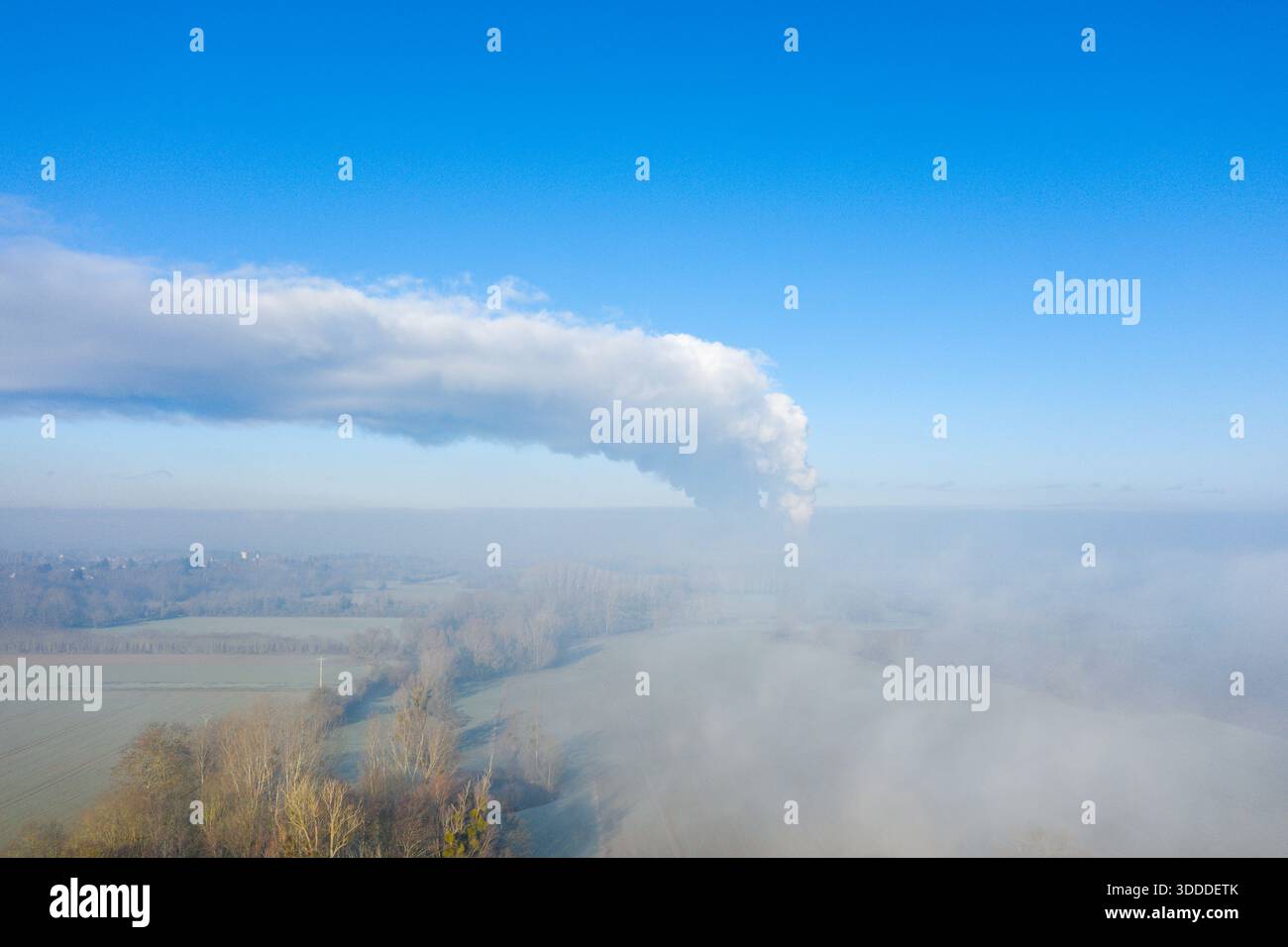 Ein schwungvoller weißer Dampfbogen erhebt sich über nebelumhüllten Winterfeldern in der Nähe von Dampierre vor einem leuchtend blauen Himmel. Der Blick aus der Vogelperspektive hebt weiche Texturen, klares Licht und eine ruhige ländliche Atmosphäre hervor. Stockfoto