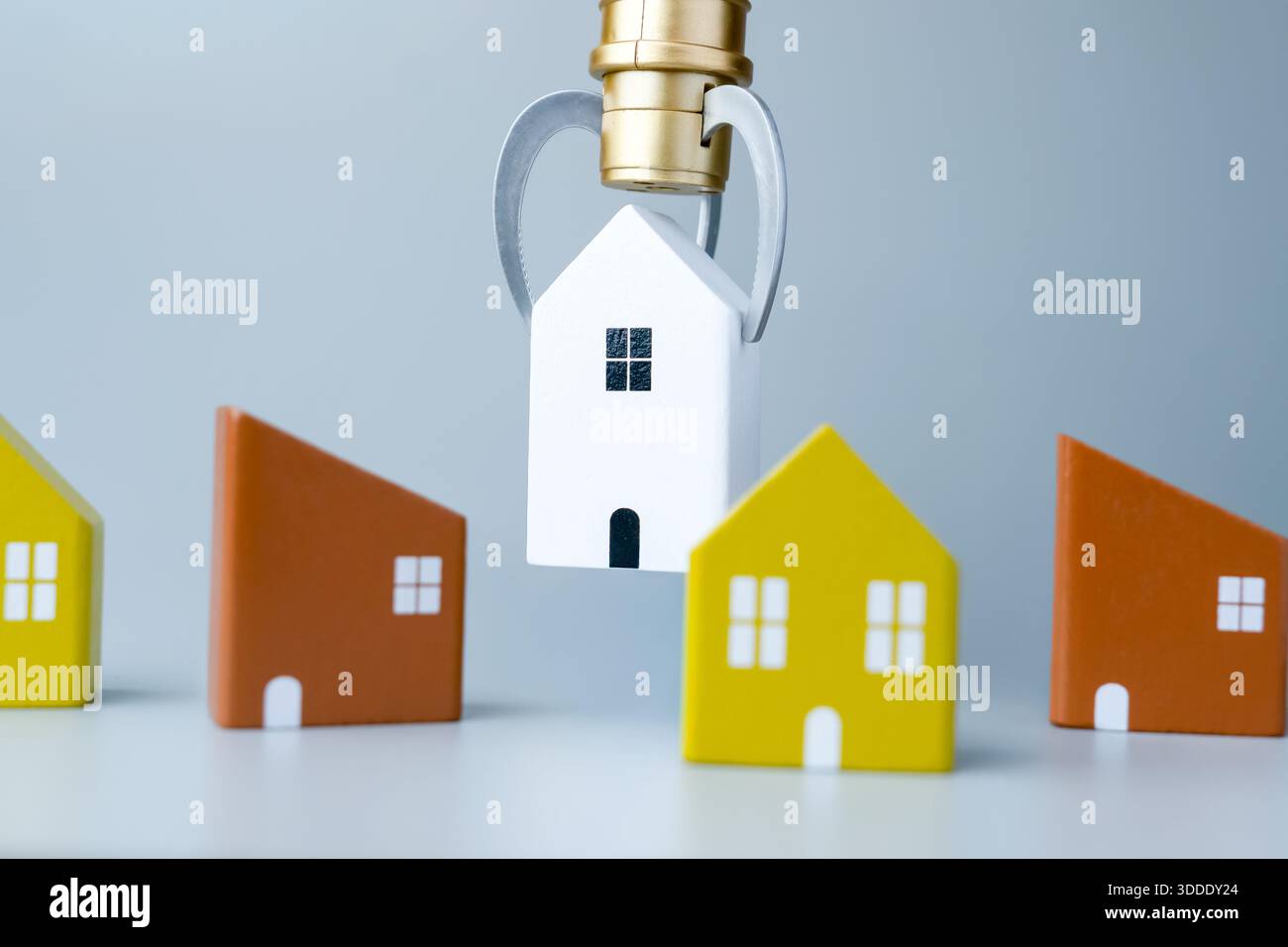 Eine Klauenmaschine, die ein kleines Hausmodell neben anderen Häusern hochhebt. Hausjagd, Hypothekenauswahl, Hauskonzept wählen. Stockfoto