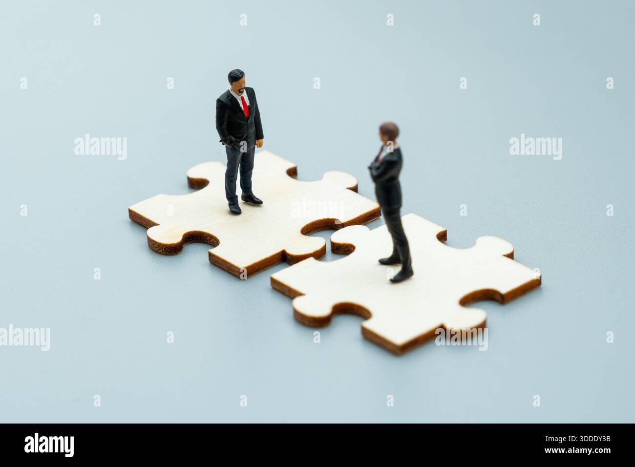 Kleine Geschäftsfiguren stehen auf ineinander greifenden Puzzleteilen. Unternehmenspartnerschaft, Teamarbeit, strategisches Collaboration-Konzept. Stockfoto