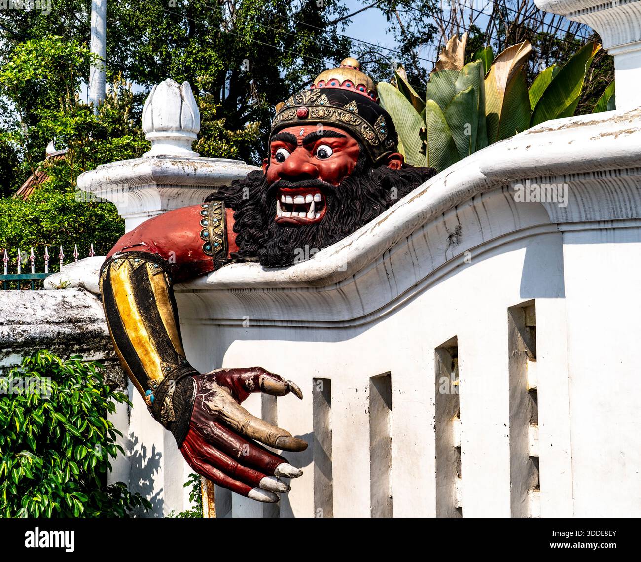Eine große, farbenfrohe Statue einer mythischen Kreatur mit einem wilden Ausdruck, ragt von einer weißen Wand, umgeben von Grün. Stockfoto