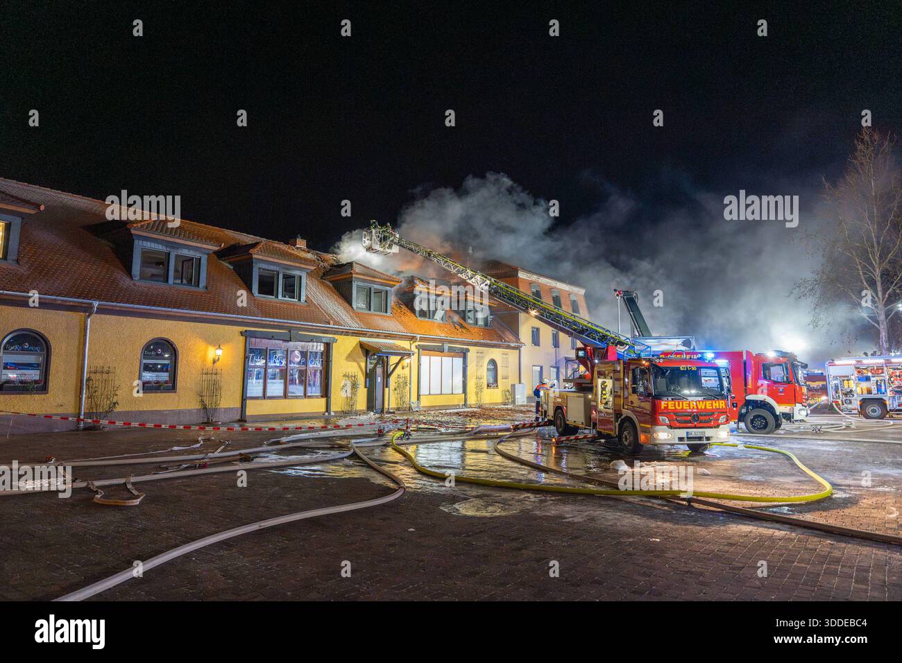 Lieferwagen brennt neben Gebäude Feuer greift auf Dachstuhl über am 31.12.2025 geriet kurz vor 02:00 Uhr ein Lieferwagen in Brand, der direkt neben einem Gebäude mit Wohn- und Geschäftseinheiten in Bickenbach Stand. Die Flammen griffen auf den angrenzenden Dachstuhl über und breiteten sich auf dem Großteil des Dachbodens aus. Da dieser nicht von innen erreichbar war, müssen die Einsatzkräfte die gesamten Dachziegel entfernen, um gezielte Löschmaßnahmen durchführen zu können. Vier Drehleitern sowie ein Mast der Werkfeuerwehr Merck kam zum Einsatz. Winterliche Minusgrade erschwerten die Lösc Stockfoto