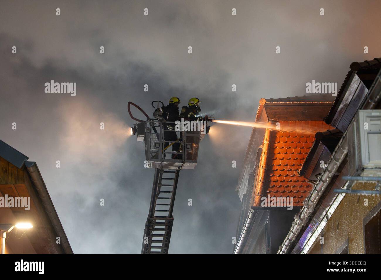 Lieferwagen brennt neben Gebäude Feuer greift auf Dachstuhl über am 31.12.2025 geriet kurz vor 02:00 Uhr ein Lieferwagen in Brand, der direkt neben einem Gebäude mit Wohn- und Geschäftseinheiten in Bickenbach Stand. Die Flammen griffen auf den angrenzenden Dachstuhl über und breiteten sich auf dem Großteil des Dachbodens aus. Da dieser nicht von innen erreichbar war, müssen die Einsatzkräfte die gesamten Dachziegel entfernen, um gezielte Löschmaßnahmen durchführen zu können. Vier Drehleitern sowie ein Mast der Werkfeuerwehr Merck kam zum Einsatz. Winterliche Minusgrade erschwerten die Lösc Stockfoto