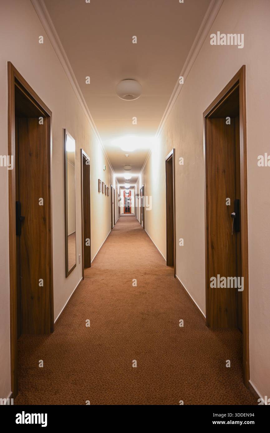 Ein leerer Hotelflur mit vielen Holztüren und beleuchteten Deckenleuchten. Stockfoto