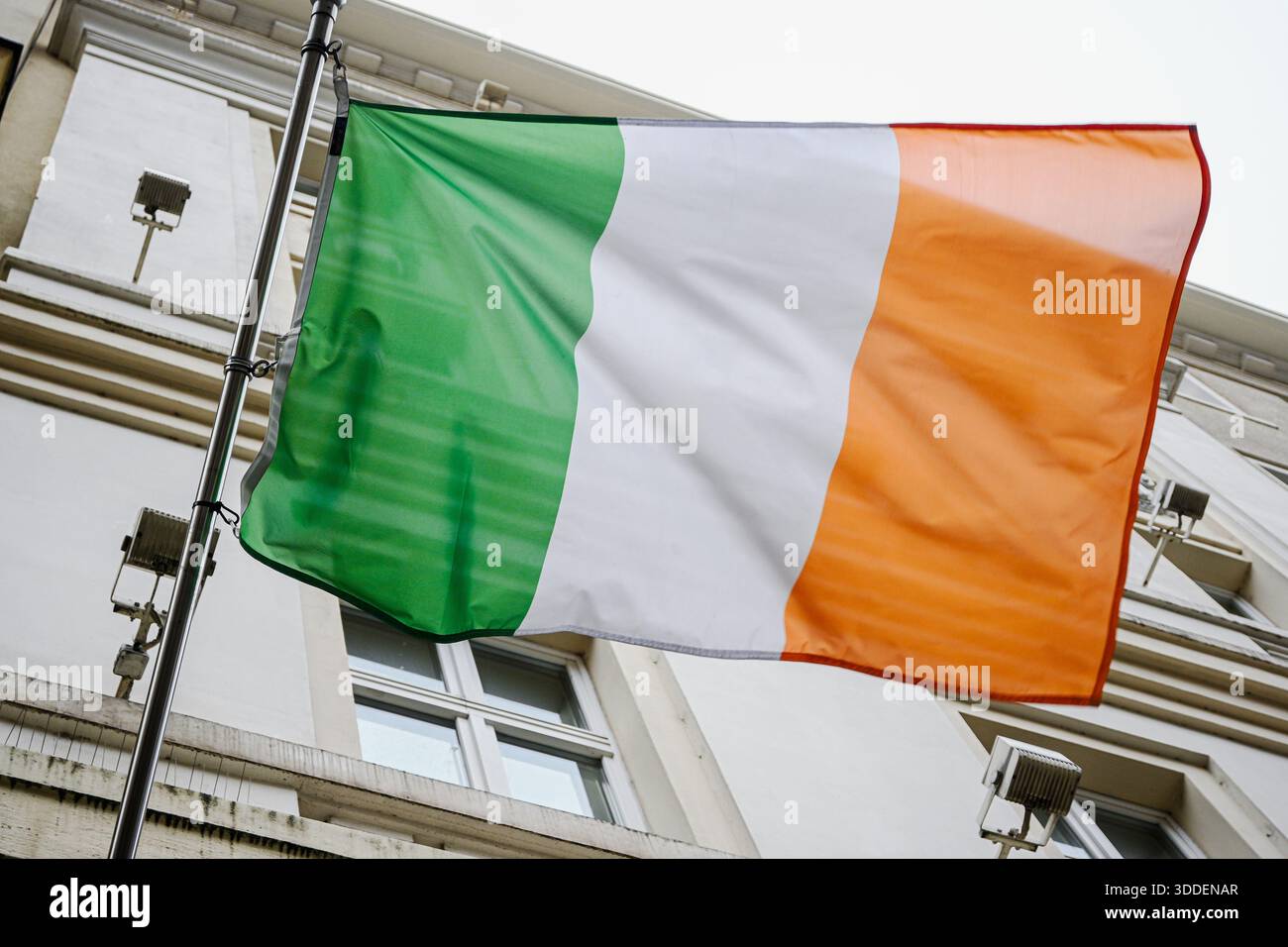 Irische Flagge mit grünen, weißen und orangen Streifen, die auf einem Fahnenmast gegen ein Gebäude fliegen. Stockfoto