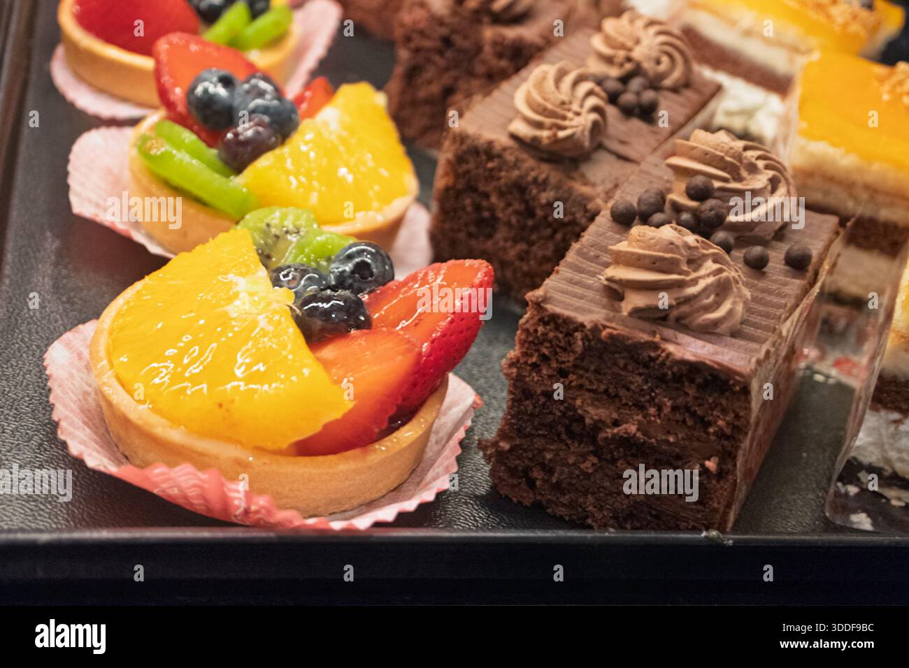 Verschiedene bunte Obstkuchen mit frischen Beeren und Zitrusfrüchten sowie reichhaltiges Schokoladengebäck für süßen Genuss Stockfoto
