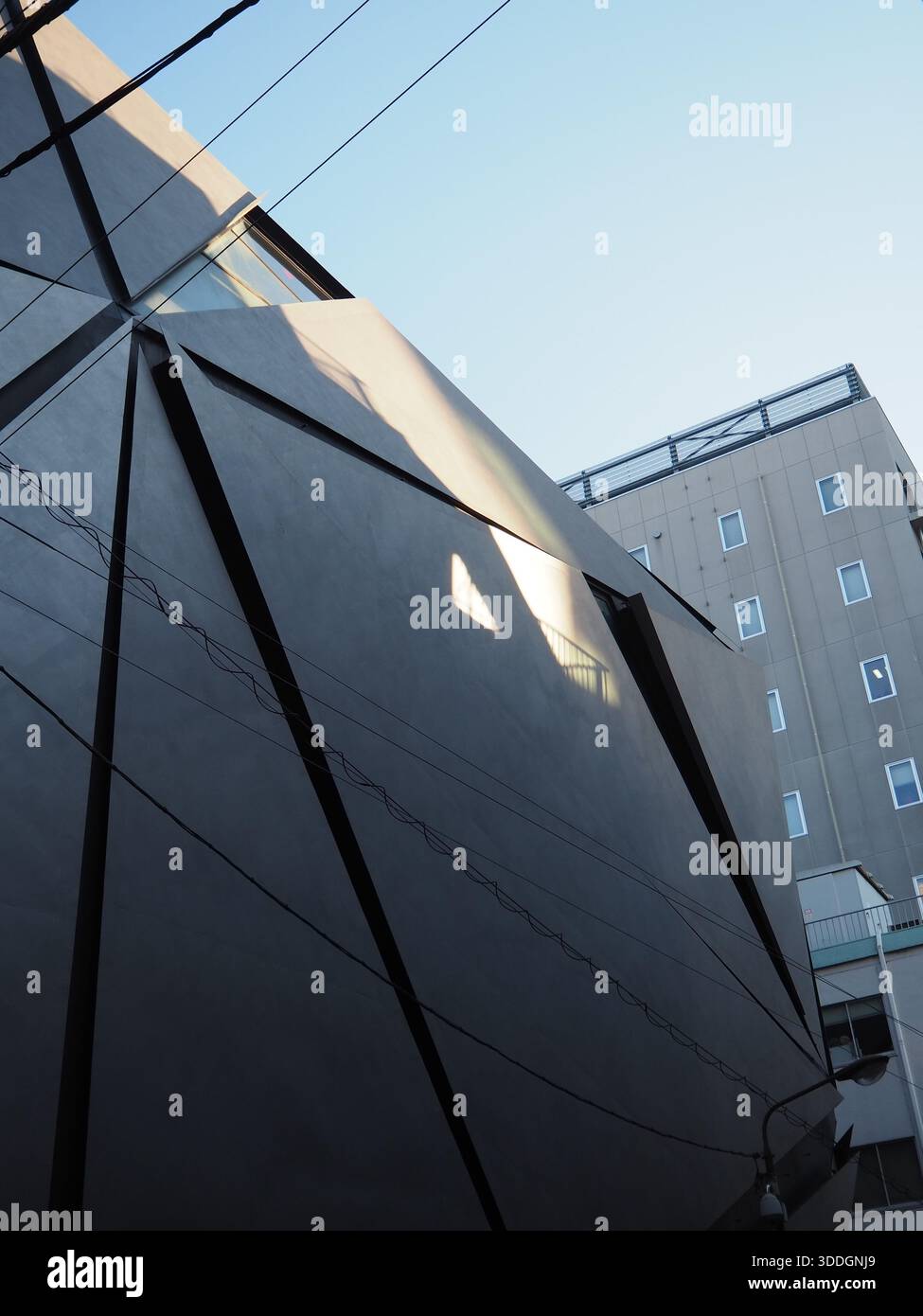 Moderne schwarze architektonische Fassade mit scharfen geometrischen Linien und Stromkabeln vor klarem blauem Himmel in Jimbocho Tokio Stockfoto