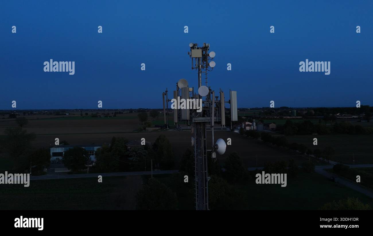 Mobilfunkturm steht vor dem dunkelblauen Himmel, ausgestattet mit verschiedenen Antennen für drahtlose Kommunikation und Mobilfunkdienste im gesamten Po Val Stockfoto