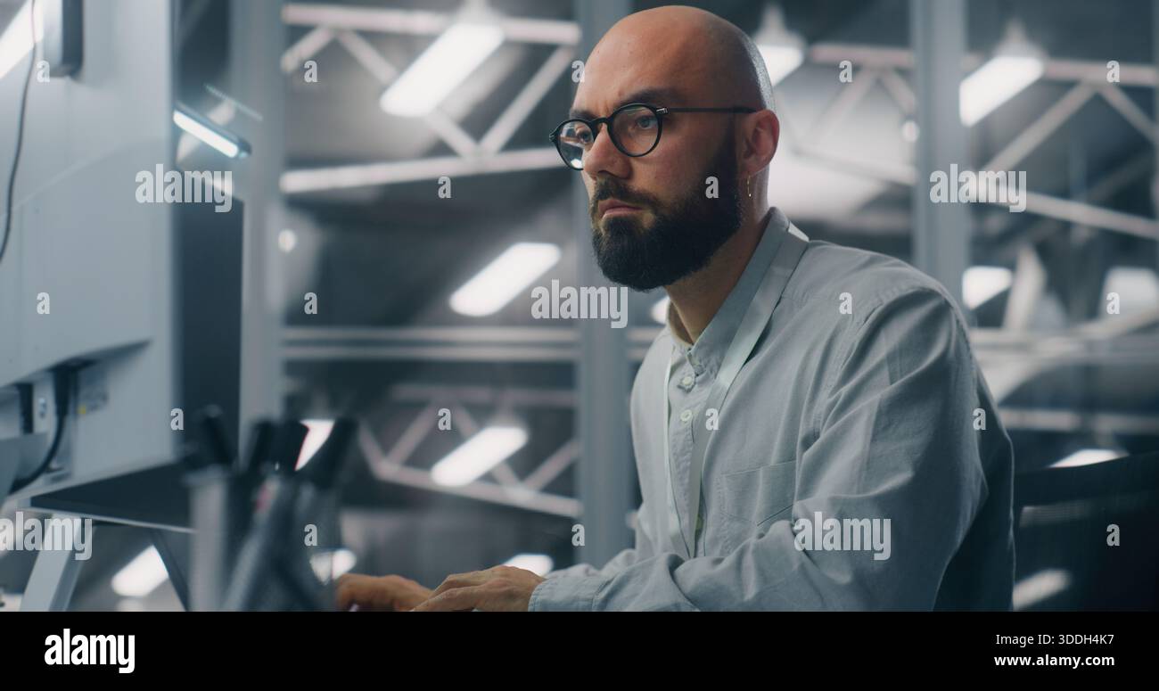 Bärtiger männlicher IT-Spezialist mit Brille, intensiv auf Computermonitore fokussiert. Hintergrundfunktionen: Coole, technische Umgebung des Serverkontrollraums. Analyse kritischer Daten und dediziertes Fachwissen. Stockfoto
