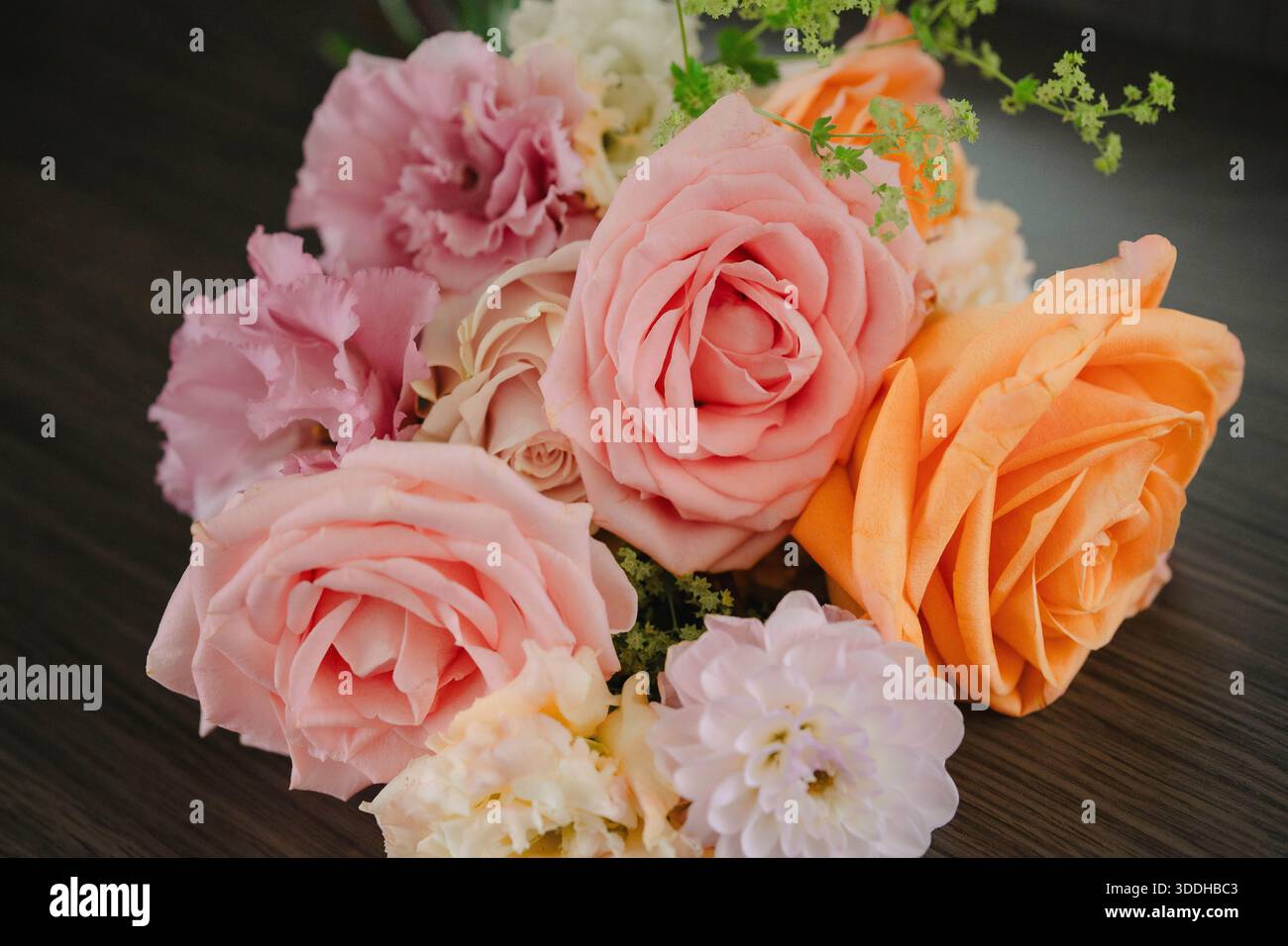 Blumenarrangements mit zarten rosa und pfirsichfarbenen Rosen und frischen grünen Akzenten, elegant auf dunkler Holzoberfläche angeordnet, schöner Blumenstrauß für Hochzeiten Stockfoto