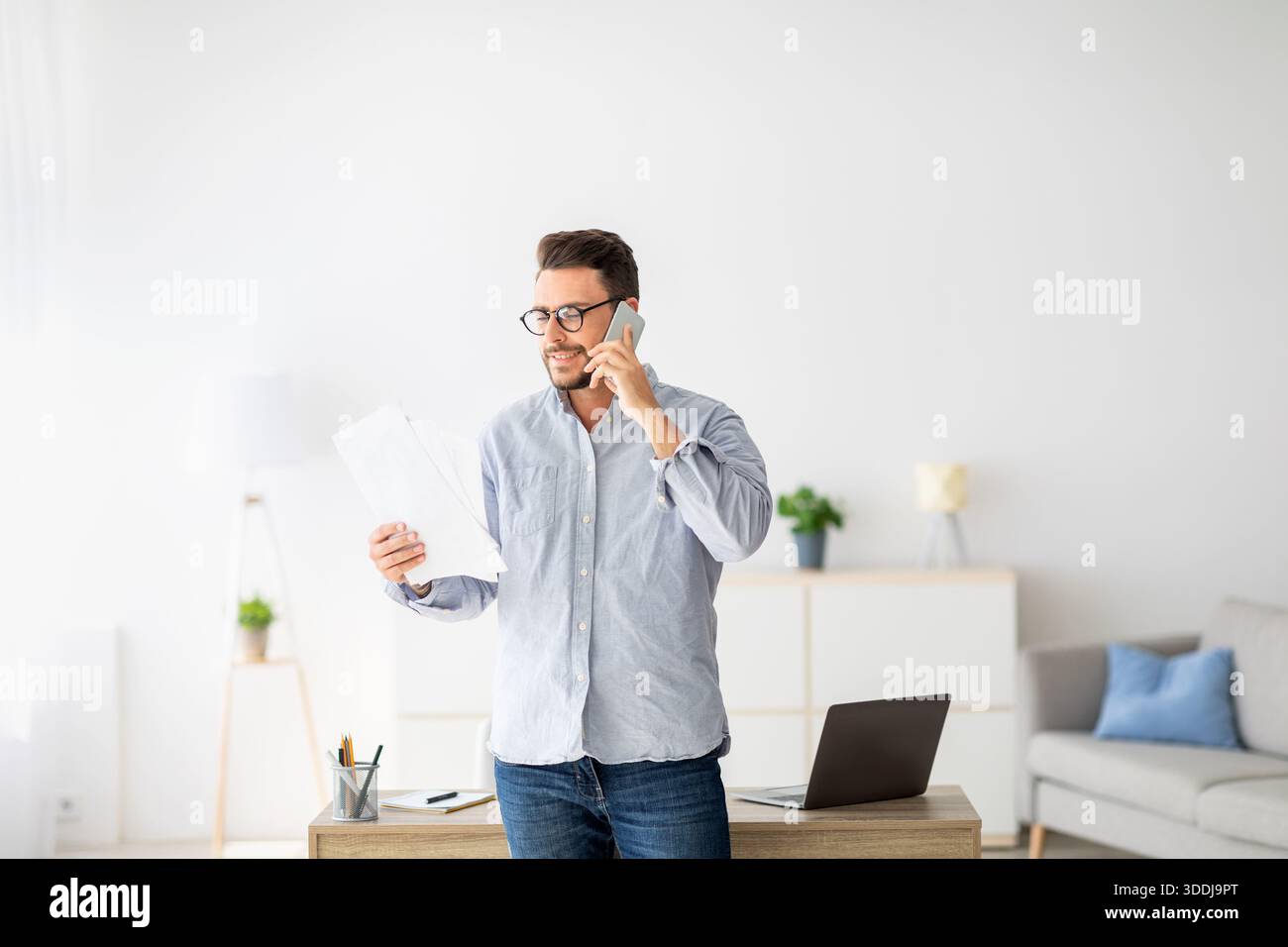 Home Office-Konzept. Selbstbewusster Millennial-Unternehmer, der am Handy spricht und Finanzberichte diskutiert Stockfoto