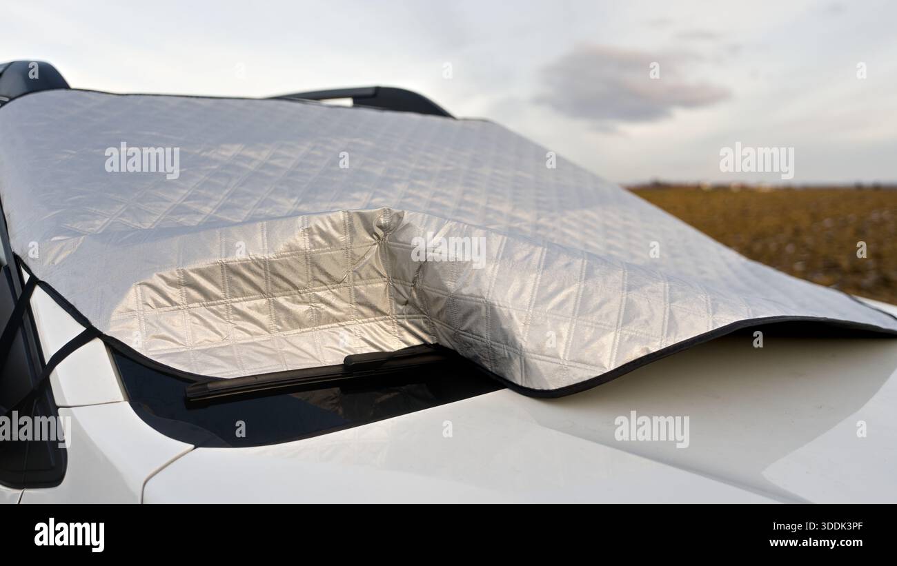 Silberne Windschutzscheibenabdeckung bei einem Auto mit einem weiten Feld im Hintergrund, das das Fahrzeug vor Sonnenlicht und Wetter schützt. Stockfoto