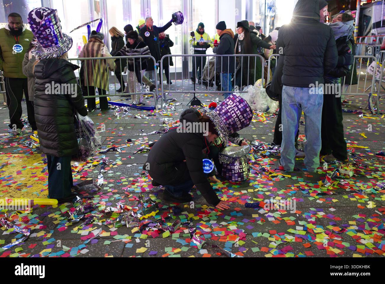 Eine geschäftige Straßenszene, die mit farbenfrohen Konfetti bedeckt ist, mit festlichen Hüten und Tragetaschen, was auf eine Umgebung nach der Feier hindeutet. Stockfoto