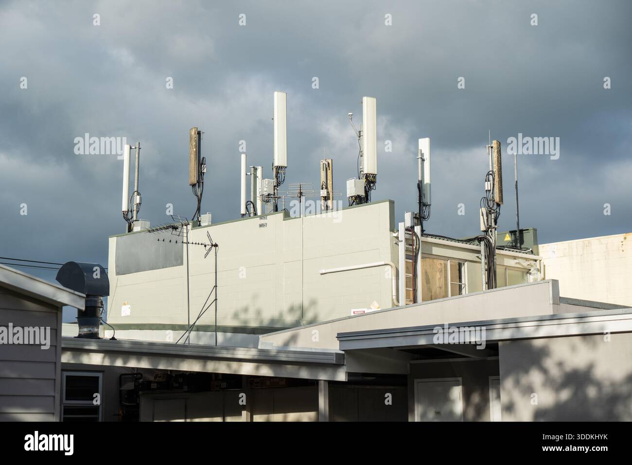 Mobiltelefontürme und Antennentafeln, die auf dem Dach eines Geschäftsgebäudes montiert sind, heben die städtische Telekommunikationsinfrastruktur hervor Stockfoto