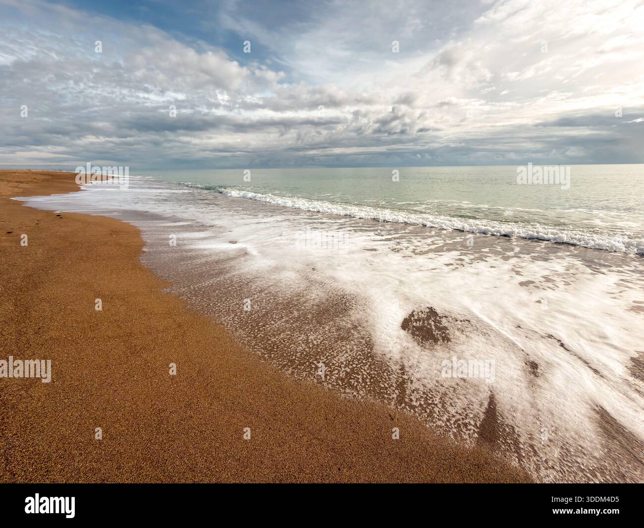 Sanfte Meereswellen, die den Sandstrand unter dramatisch bewölktem Himmel berühren Stockfoto
