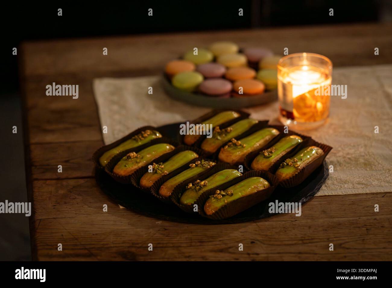 Pistazien-glasierte Eclairs werden auf einem rustikalen Tisch bei Kerzenschein an einem eleganten Dessertbuffet serviert. Gourmet-Pistazien-Eclairs arrangierten für eine Luxusveranstaltung. Stockfoto