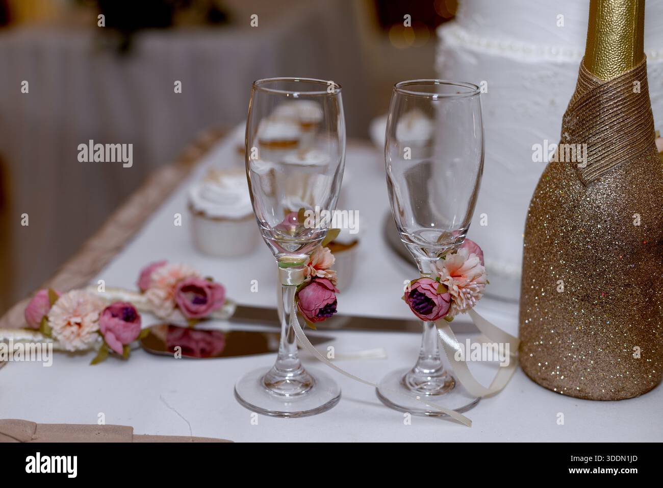 Elegante Sektflöten zur Hochzeit mit Blumen und Glitzerflaschen im Hintergrund Stockfoto
