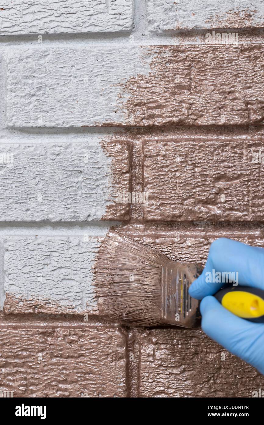 Person, die mit einem Pinsel eine graue Ziegelwand mit roségoldfarbener Metallic-Farbe übermalt. Machen Sie es sich selbst nach Hause Verbesserungskonzept. Stockfoto