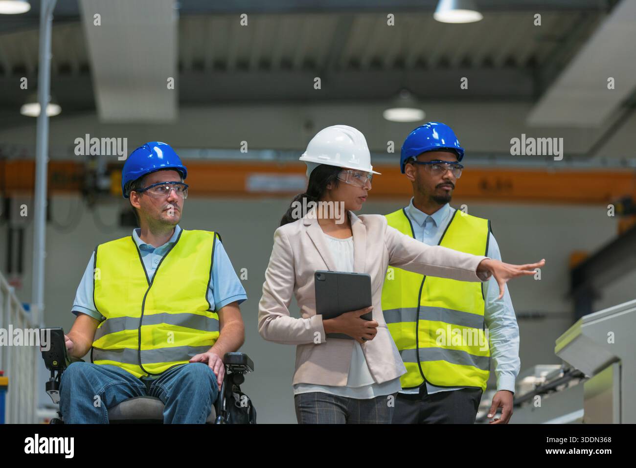 Weibliche Führungskraft spricht mit zwei Arbeitern an der Produktionslinie, darunter einer mit Behinderung, über den Produktionsprozess. Stockfoto