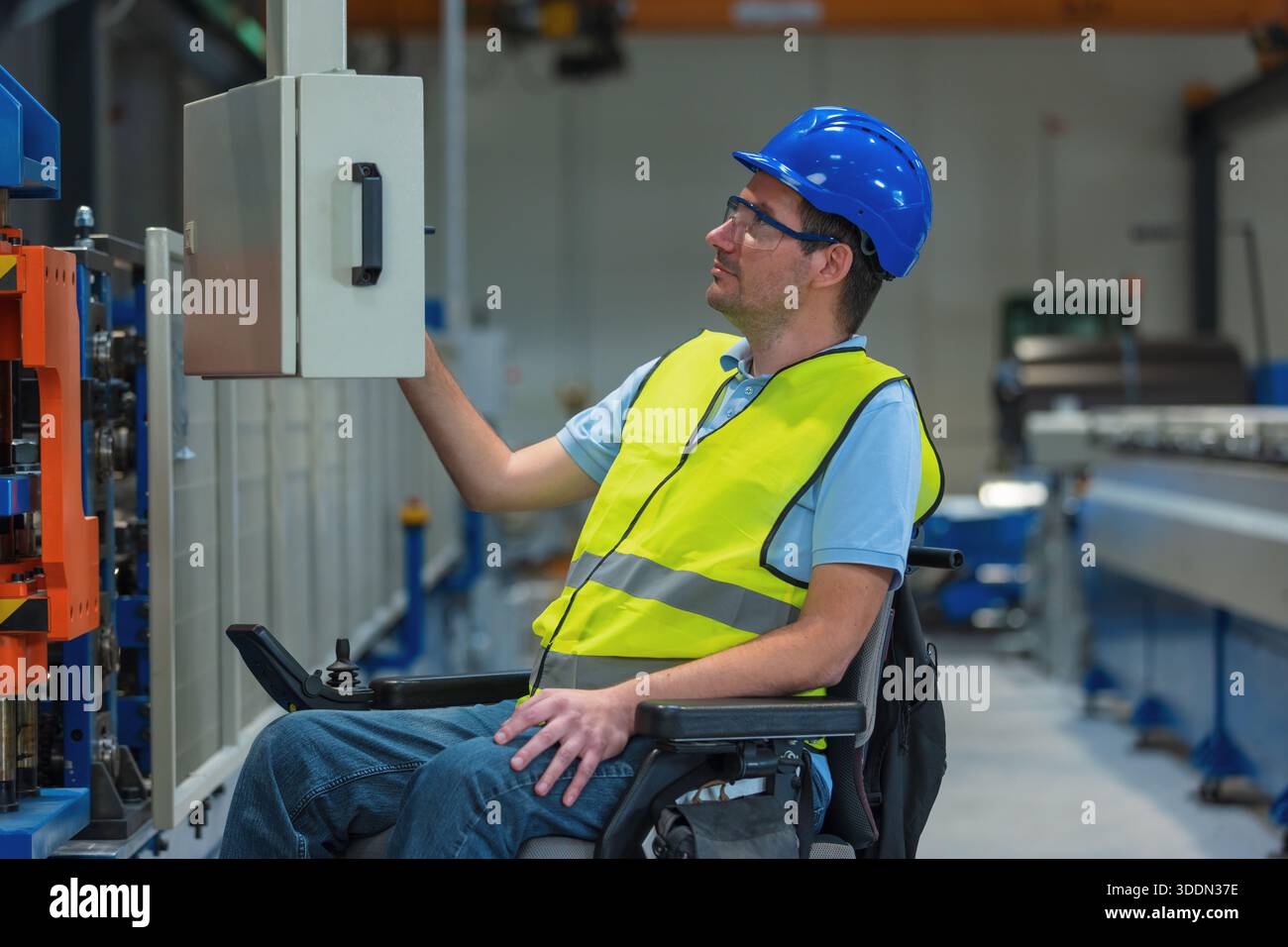 Fertigungsingenieur mit Behinderung in einer Fabrik mit gelber Weste und blauem Helm bei der Arbeit. Stockfoto
