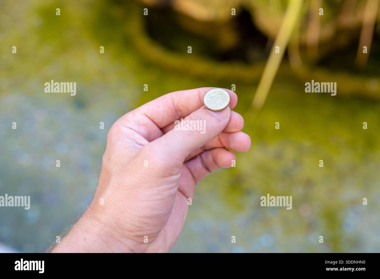 Die Hand eines Mannes, der einen 10 Cent Euro in einen Brunnen wirft, um sich etwas zu wünschen Stockfoto