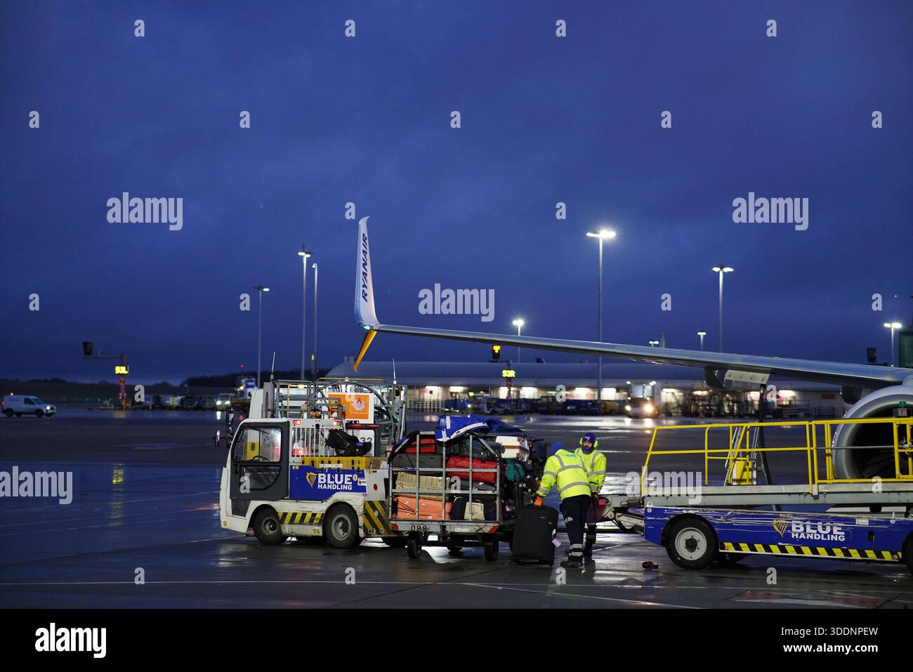 Flughafenbodenbesatzung, die Gepäck bei regnerischen Bedingungen am frühen Morgen neben einem Ryanair-Flugzeugflügel verlädt. Budapest, Ungarn Stockfoto