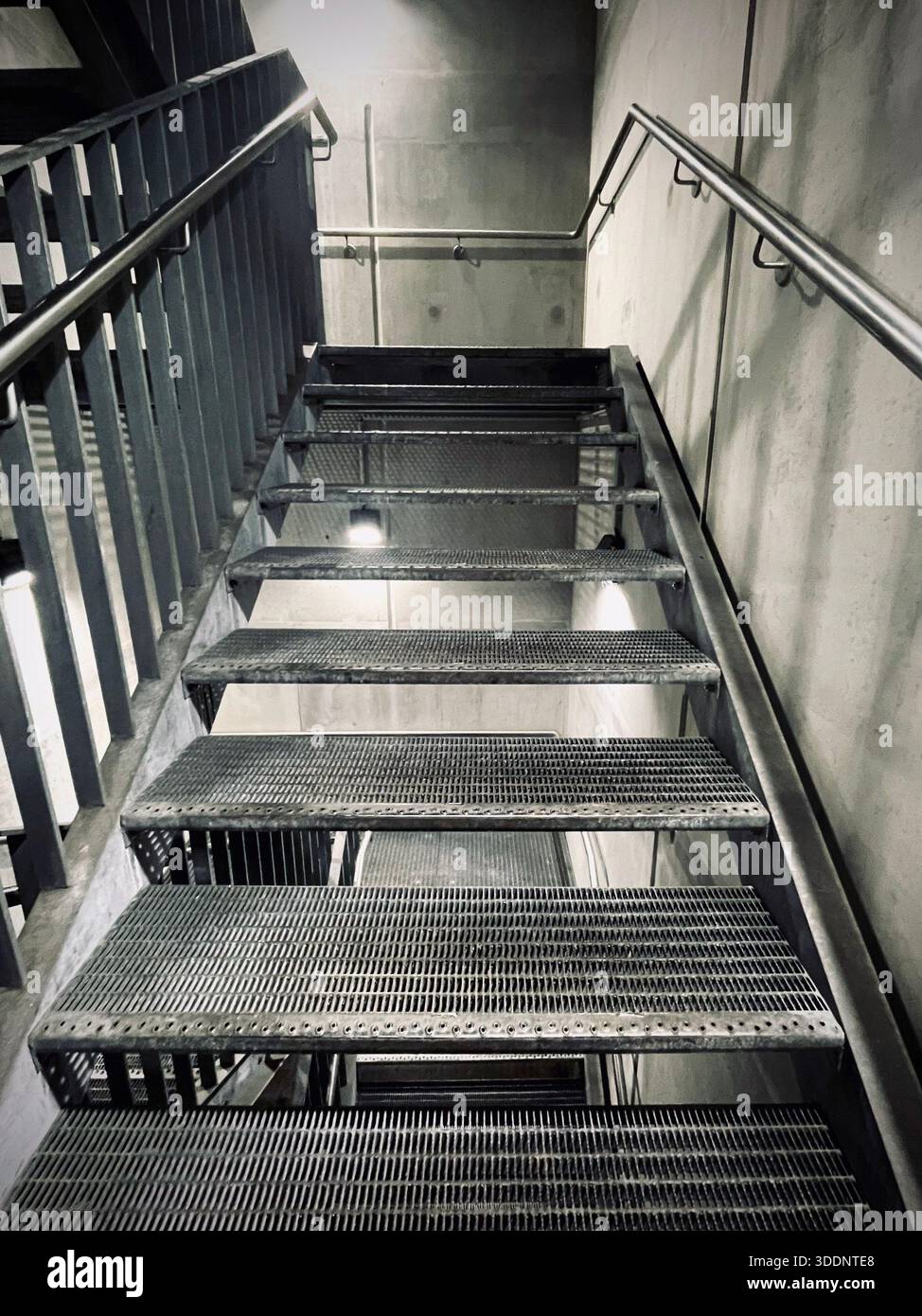 Industrielle Metalltreppe mit Gittertreppen und Edelstahlgeländern in einem modernen Gebäude, mit Blick auf eine abstrakte architektonische Rückseite - Smartphone-aufgenommenes Stockfoto