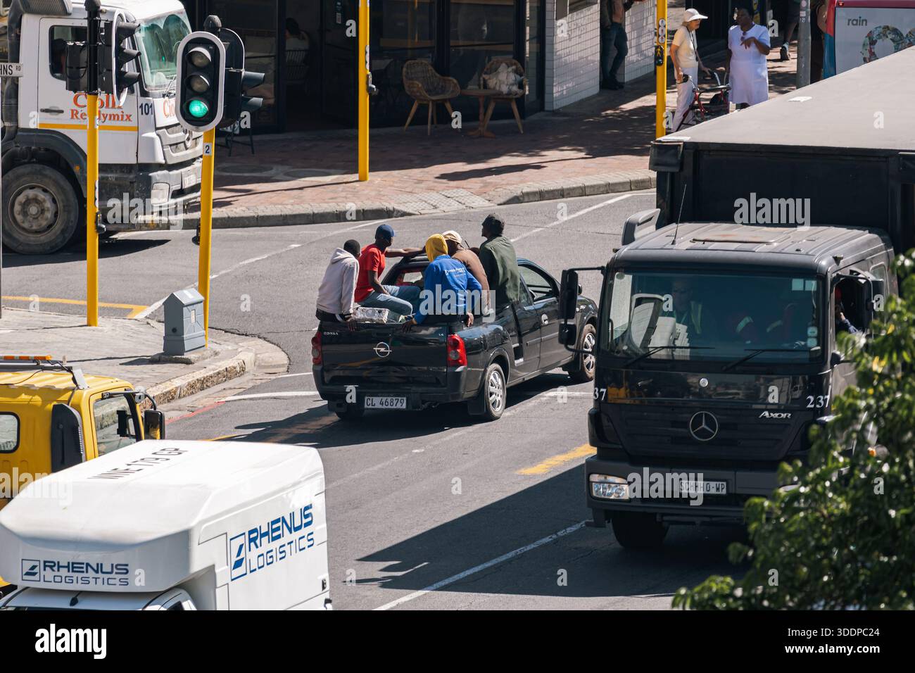 Männer fahren auf der offenen Rückseite eines Pickup-Trucks entlang einer Stadtstraße, unter städtischen Verkehrsbedingungen. Verstöße gegen Transport- und Verkehrsvorschriften. Kap Stockfoto