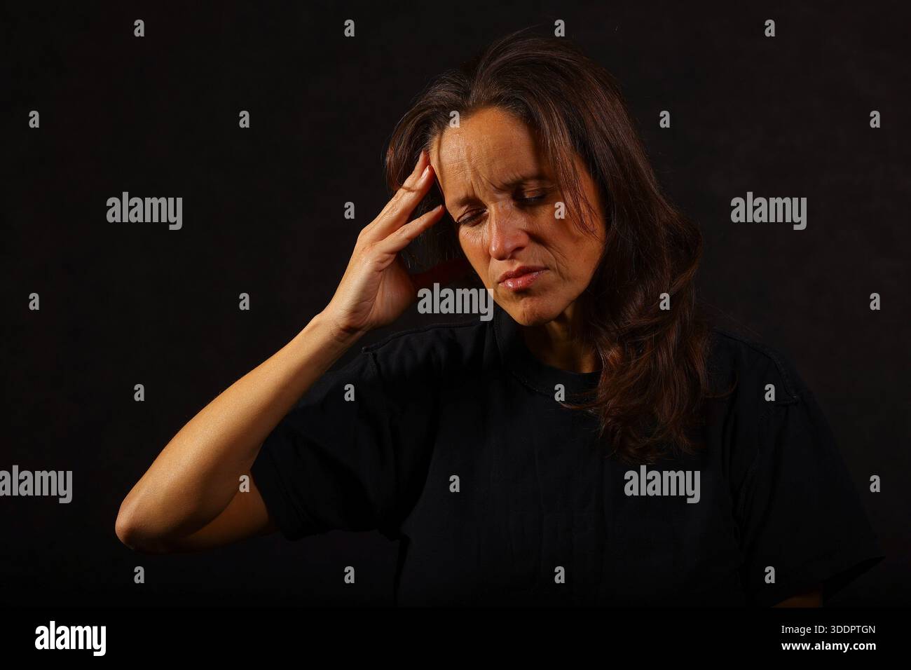 Frau, die ihren Tempel berührt, Frustration, Stress oder emotionale Schmerzen zeigt. Dunkler Hintergrund, dramatisches Licht, psychische Gesundheit und psychologisches Konzept Stockfoto