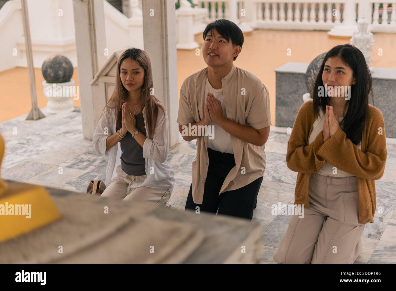 Junge asiatische Menschen knieten mit Händen in Gebetsgesten, üben spirituelle Hingabe in einem Tempel Stockfoto