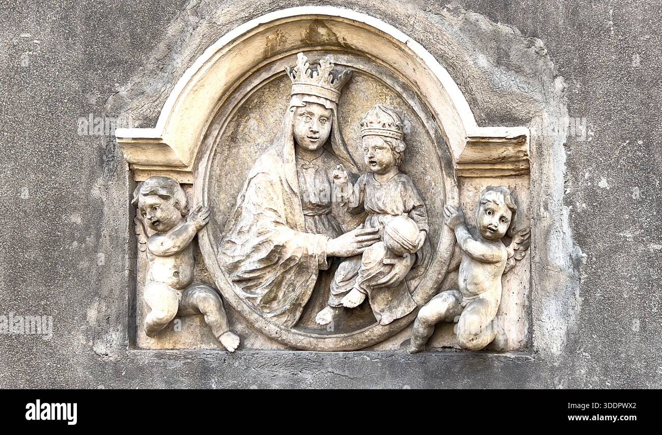 Madonna und Kind tragen Kronen, flankiert von zwei Engeln in einem alten Steinrelief Stockfoto