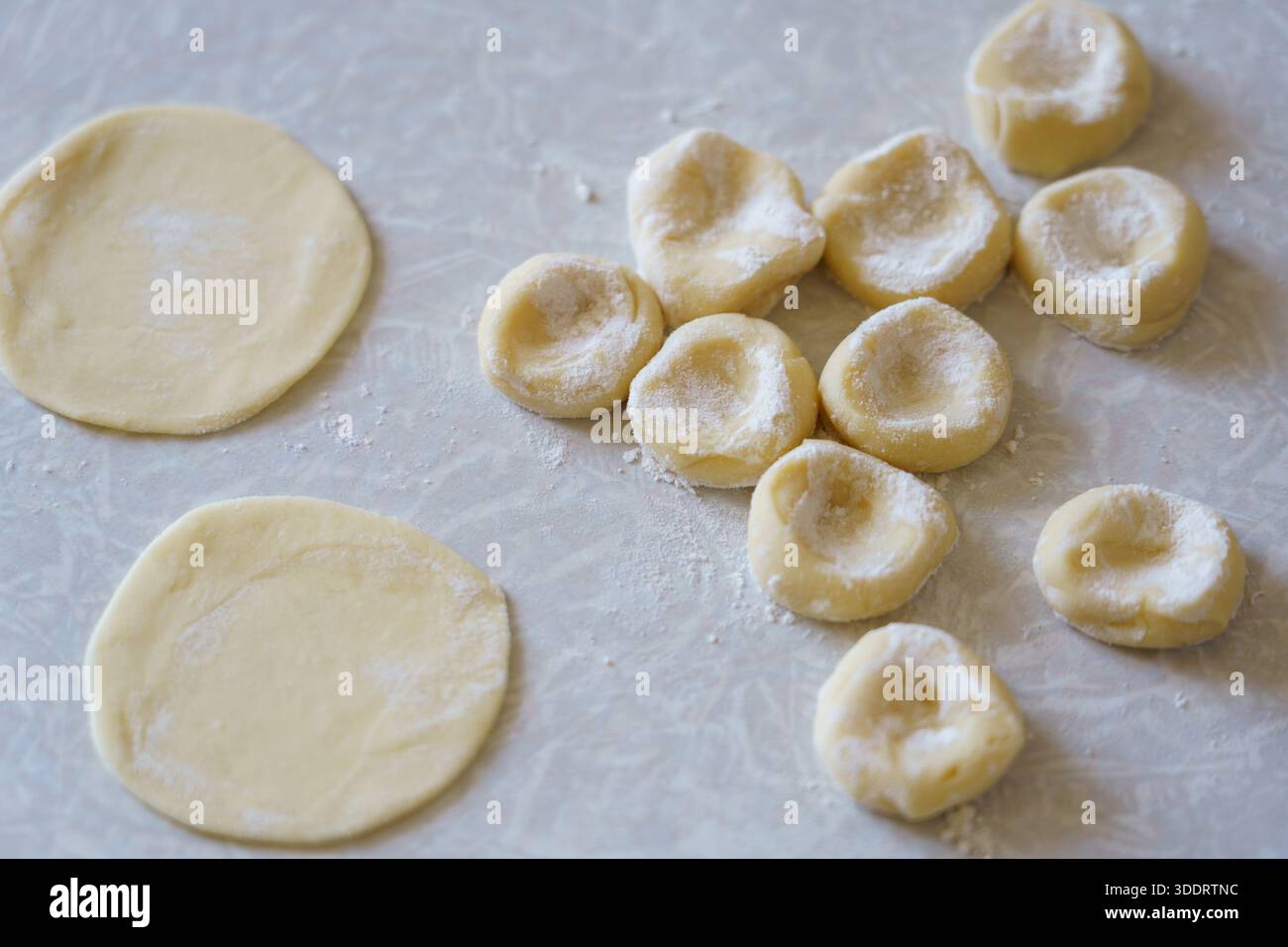 Teigkreise werden auf einer Oberfläche ausgerollt und zu kleinen Nudelstücken geformt. Diese Aktivität findet in einer Küche statt. Stockfoto