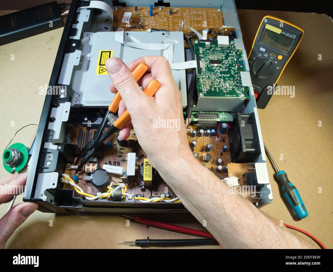 Handprüfung der elektronischen Leiterplatte mit Multimeter; Nahaufnahme der Hände des Technikers mit Hilfe eines Multimeters zur Diagnose oder Reparatur komplexer elektronischer Schaltungen Stockfoto