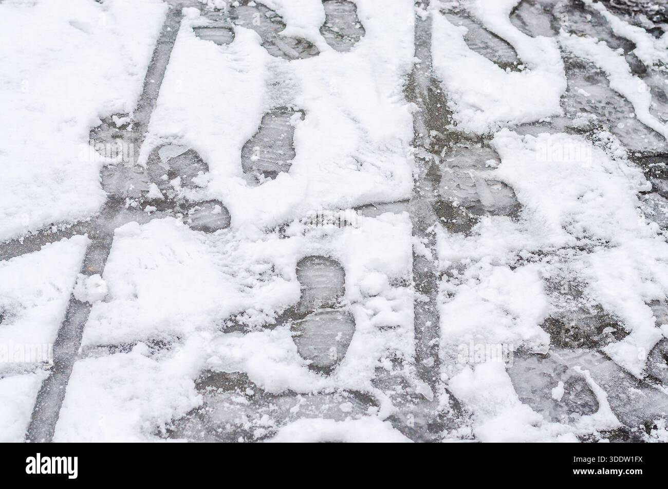 Fußabdrücke auf einem mit Gitter verzierten Steinpflaster, der mit Schnee bedeckt ist. Stockfoto