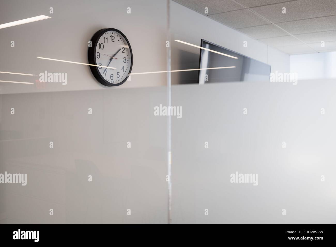 Eine minimalistische Wanduhr, die über einem Milchglasfenster in einem modernen, neu errichteten Bürogebäude montiert ist. Stockfoto