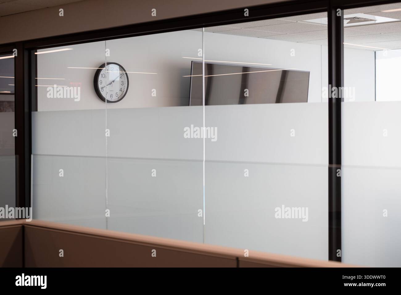Eine minimalistische Wanduhr, die über einem Milchglasfenster in einem modernen, neu errichteten Bürogebäude montiert ist. Stockfoto
