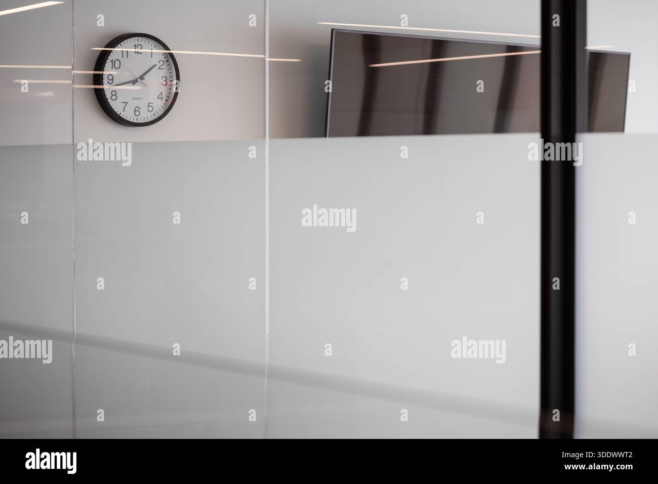 Eine minimalistische Wanduhr, die über einem Milchglasfenster in einem modernen, neu errichteten Bürogebäude montiert ist. Stockfoto