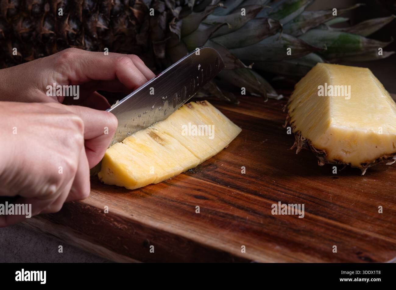 Eine Ananas mit einem Messer auf einem Holzschneidebrett in Scheiben schneiden Stockfoto