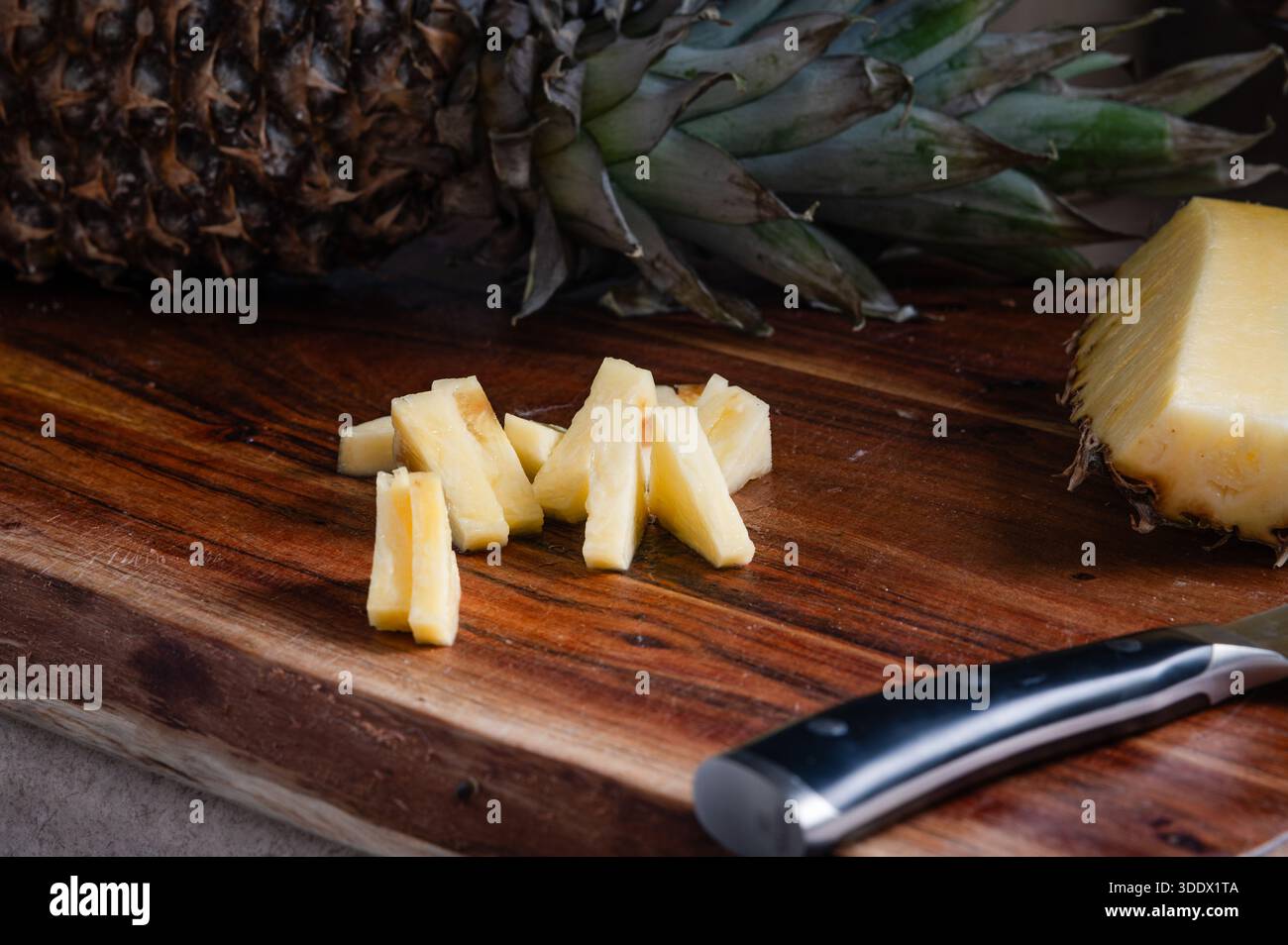 Ananasscheiben auf einem Holzschneidebrett mit einer ganzen Ananas im Hintergrund Stockfoto
