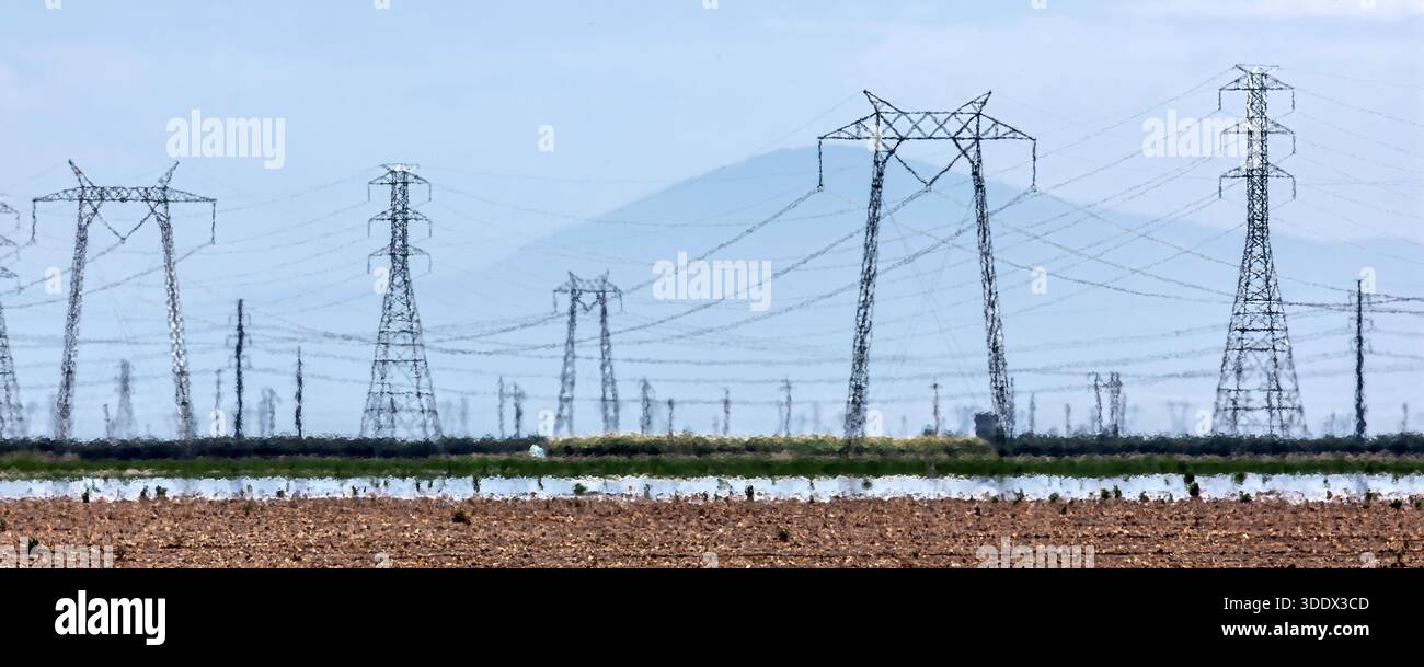Wenn man über ein heißes landwirtschaftliches Tal blickt, scheinen Hochspannungstürme aufgrund der starken atmosphärischen Brechung über dem zu schimmern und zu verformen Stockfoto