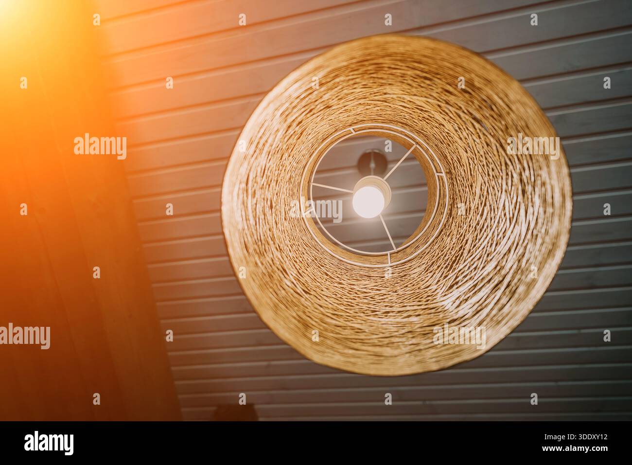 Eine rustikale Korbleuchte hängt an einer Holzdecke und schafft eine warme und einladende Atmosphäre. Stockfoto